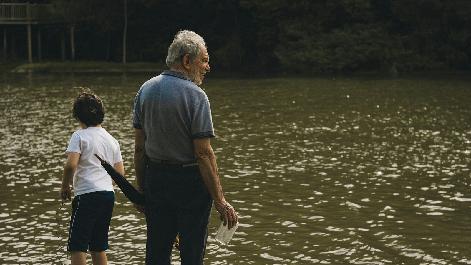 A man and a boy standing together at the edge of a lake